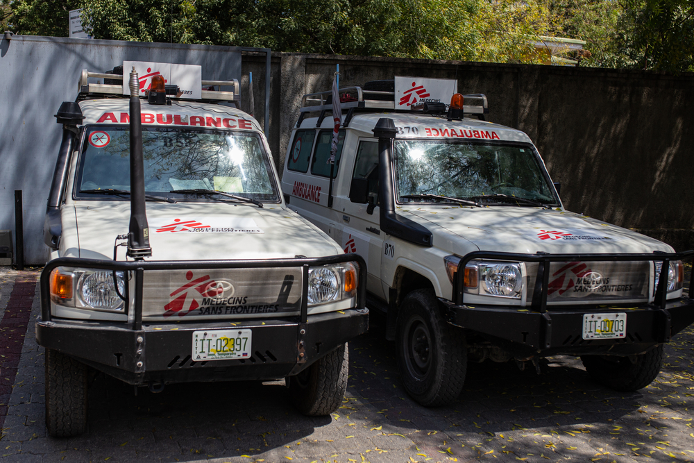 Two MSF ambulances parked under a tree shade at the MSF Emergency Center of Turgeau.