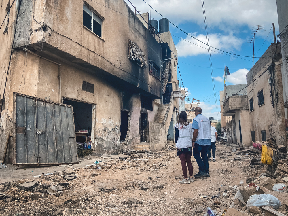 2 MSF team members standing in front of a burnt house surrounded by damaged houses in Jenin.