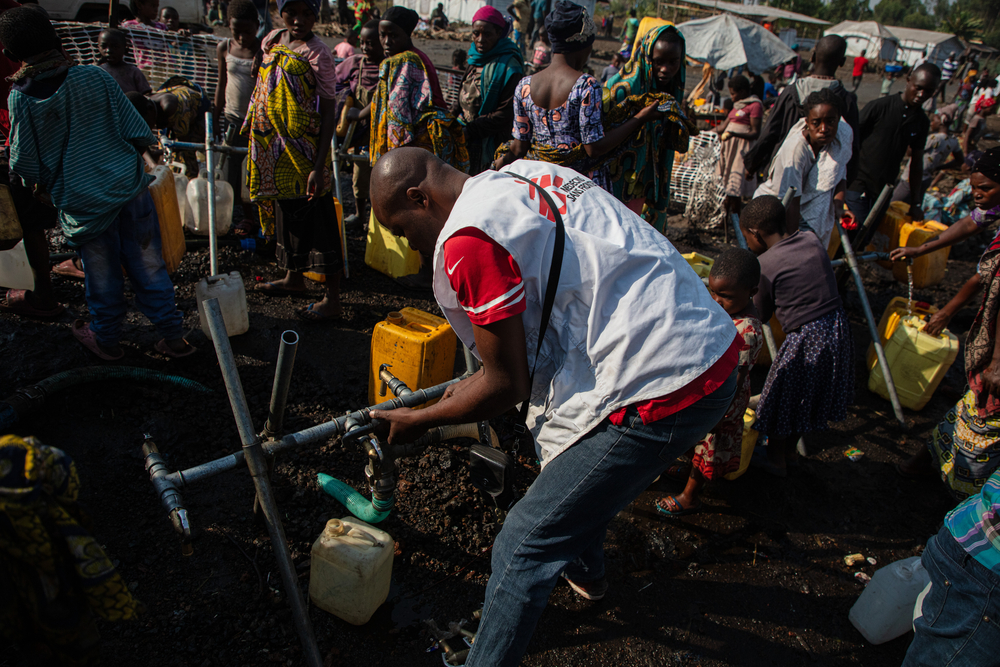 MSF staff fastening the water tap as other people collect water.